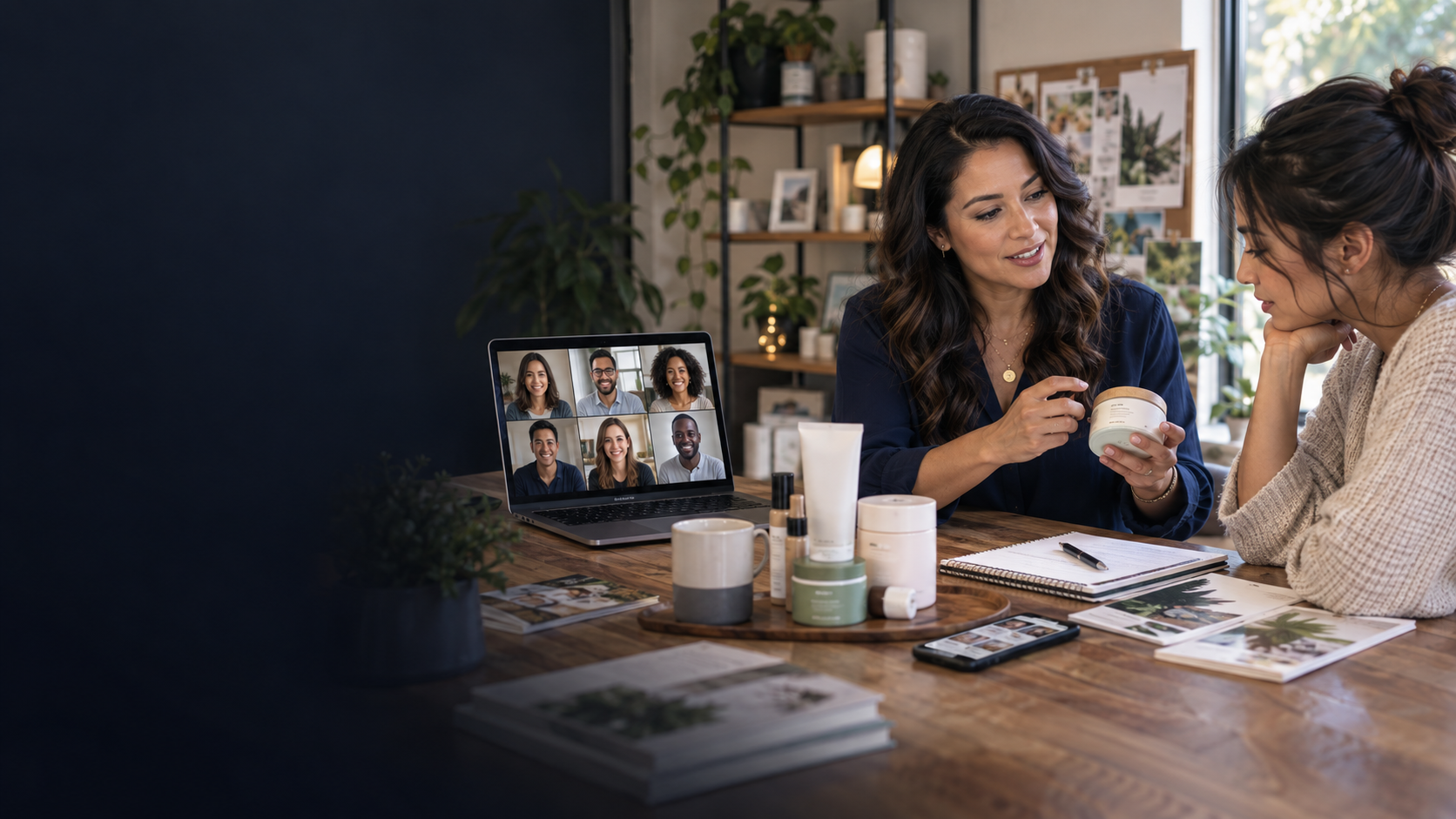 Independent consultant showing a skincare product to an interested customer at a table while a laptop displays a live team video call